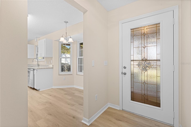 foyer with a notable chandelier, light hardwood / wood-style floors, sink, and a textured ceiling