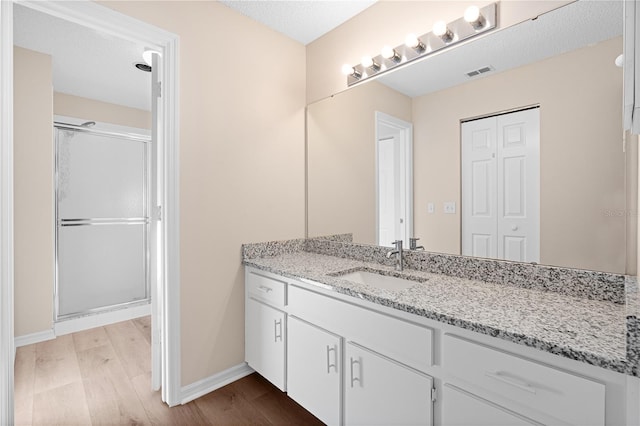 bathroom with a shower with door, vanity, wood-type flooring, and a textured ceiling