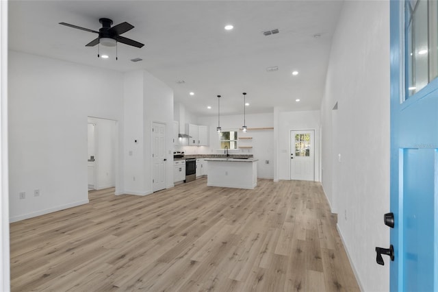 unfurnished living room with ceiling fan, light hardwood / wood-style floors, a towering ceiling, and sink