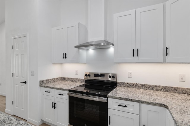 kitchen featuring light stone counters, white cabinetry, stainless steel electric stove, and wall chimney range hood