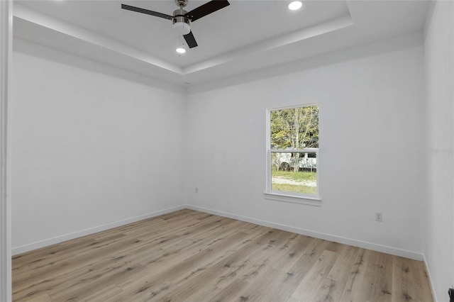 unfurnished room featuring a tray ceiling, ceiling fan, and light wood-type flooring