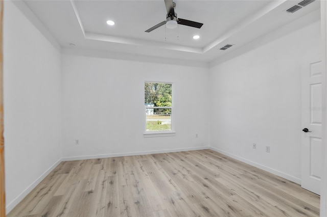 empty room with a tray ceiling, ceiling fan, and light wood-type flooring