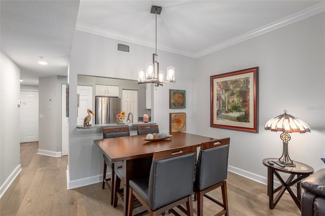 dining space with light hardwood / wood-style floors, ornamental molding, and an inviting chandelier