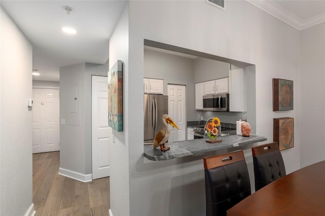 kitchen with white cabinets, wood-type flooring, crown molding, kitchen peninsula, and stainless steel appliances