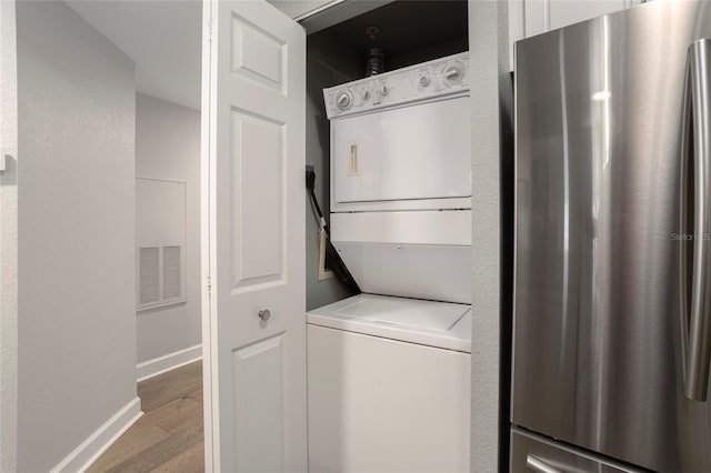 laundry area featuring stacked washer / dryer and light hardwood / wood-style flooring