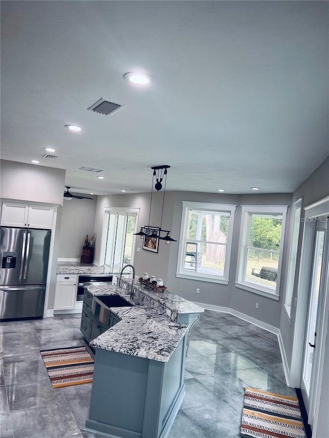 kitchen with sink, hanging light fixtures, stainless steel fridge, a kitchen island with sink, and white cabinets