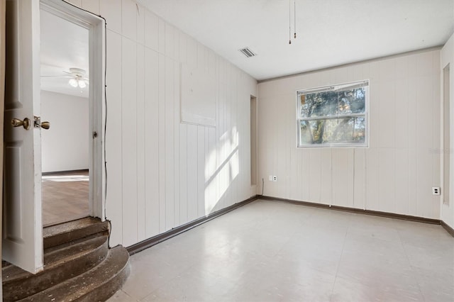 unfurnished room with ceiling fan and wooden walls