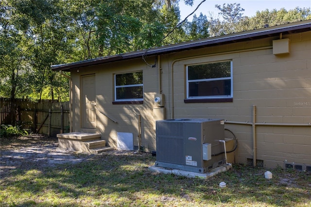 exterior space featuring concrete block siding, fence, and central air condition unit