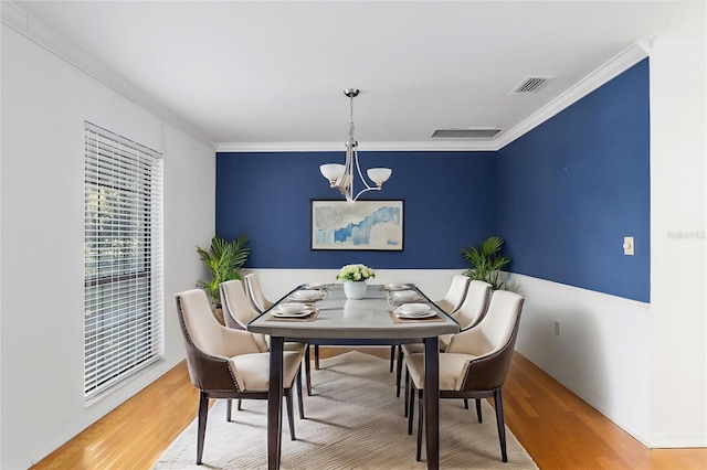 dining area featuring wood-type flooring, ornamental molding, and a chandelier