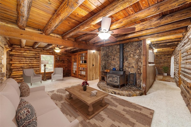 carpeted living room with a wood stove, ceiling fan, rustic walls, and beamed ceiling