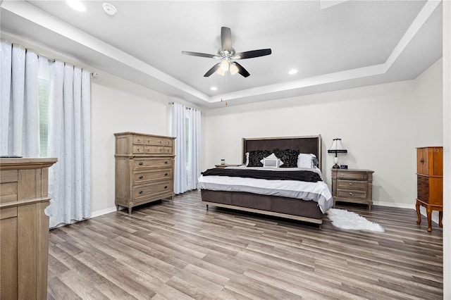 bedroom with a raised ceiling, ceiling fan, and light hardwood / wood-style flooring