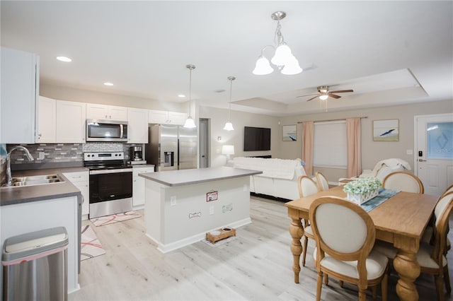 kitchen featuring sink, light hardwood / wood-style floors, decorative light fixtures, a tray ceiling, and appliances with stainless steel finishes