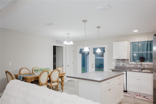 kitchen featuring backsplash, light hardwood / wood-style flooring, dishwasher, white cabinetry, and hanging light fixtures