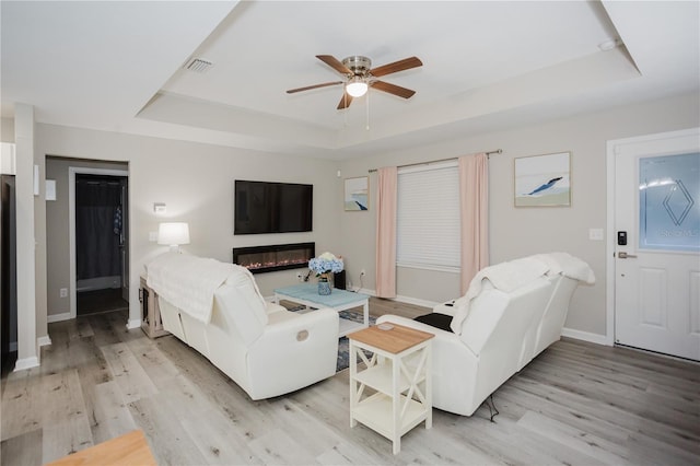 living room featuring a raised ceiling, ceiling fan, and light hardwood / wood-style floors