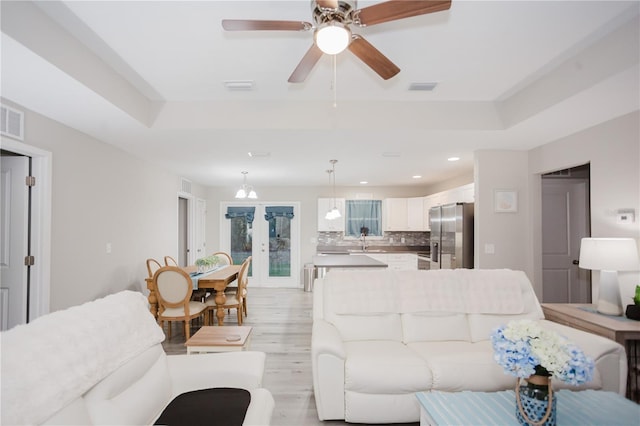 living room featuring ceiling fan, sink, french doors, a tray ceiling, and light wood-type flooring