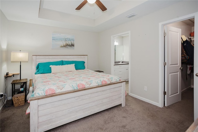 bedroom with carpet floors, ensuite bathroom, a tray ceiling, and ceiling fan