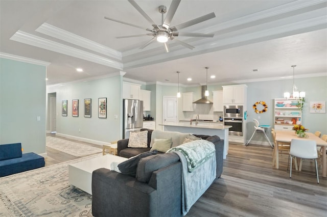 living room featuring ceiling fan with notable chandelier, hardwood / wood-style flooring, a raised ceiling, and ornamental molding