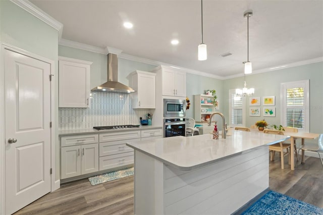 kitchen featuring wall chimney exhaust hood, hanging light fixtures, stainless steel appliances, hardwood / wood-style floors, and white cabinets