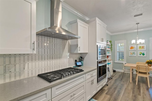 kitchen featuring white cabinets, wall chimney exhaust hood, ornamental molding, and appliances with stainless steel finishes