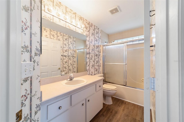 full bathroom featuring hardwood / wood-style floors, vanity, toilet, and bath / shower combo with glass door