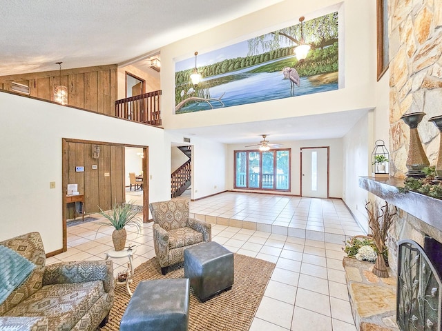 tiled living room featuring ceiling fan, a stone fireplace, high vaulted ceiling, and a textured ceiling