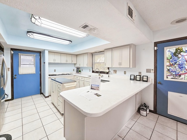 kitchen with a raised ceiling, light tile patterned flooring, a textured ceiling, and kitchen peninsula