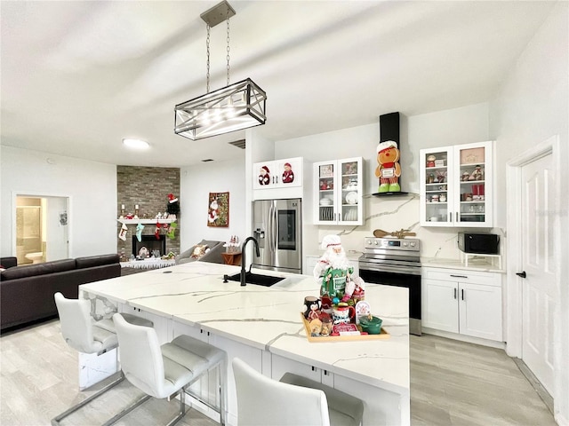 kitchen featuring appliances with stainless steel finishes, sink, exhaust hood, decorative light fixtures, and light hardwood / wood-style floors