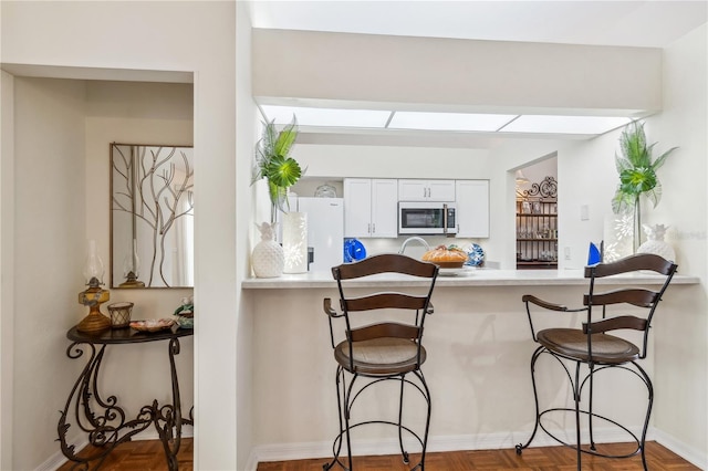 kitchen featuring parquet floors, a kitchen breakfast bar, white refrigerator with ice dispenser, kitchen peninsula, and white cabinets