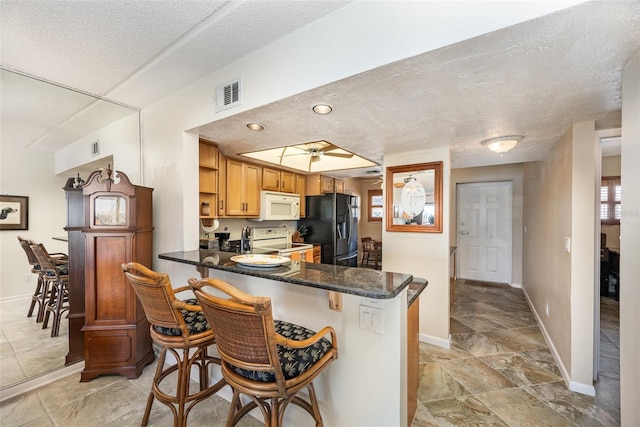 kitchen with kitchen peninsula, a textured ceiling, white appliances, and a breakfast bar