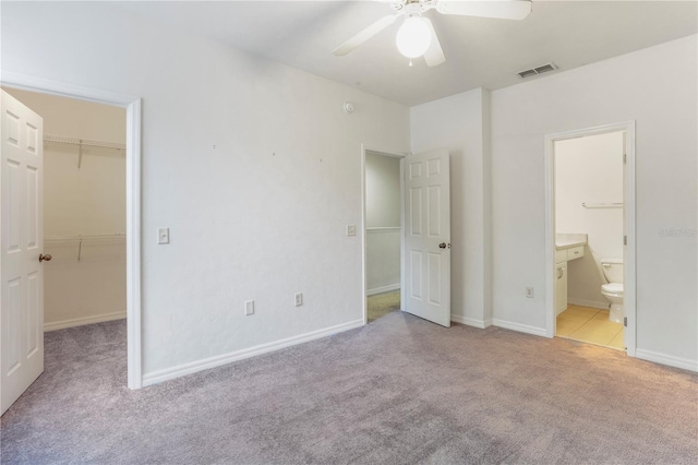 unfurnished bedroom with a walk in closet, ceiling fan, a closet, and light colored carpet