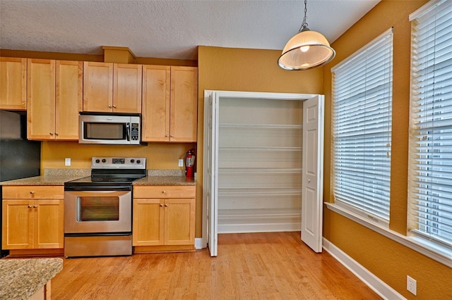 kitchen featuring appliances with stainless steel finishes, light wood-type flooring, pendant lighting, and a healthy amount of sunlight