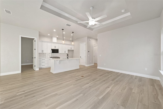 unfurnished living room featuring sink, a tray ceiling, and light hardwood / wood-style flooring