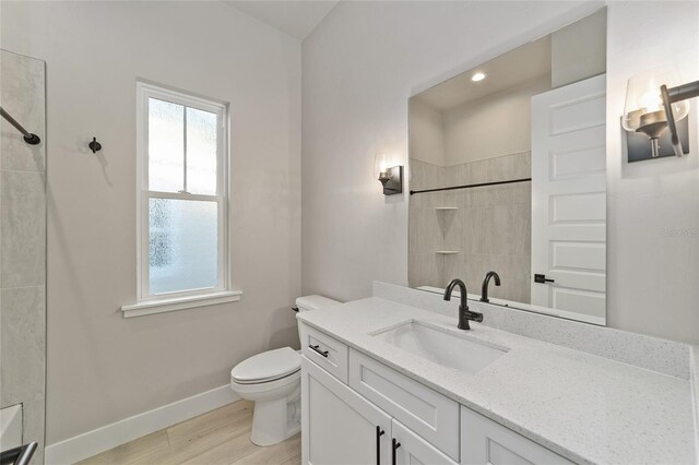 bathroom with hardwood / wood-style floors, vanity, toilet, and tiled shower