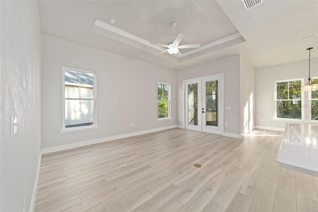 empty room featuring a tray ceiling, light hardwood / wood-style flooring, a healthy amount of sunlight, and french doors