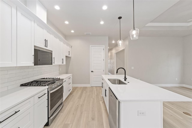 kitchen with hanging light fixtures, sink, an island with sink, appliances with stainless steel finishes, and light hardwood / wood-style floors