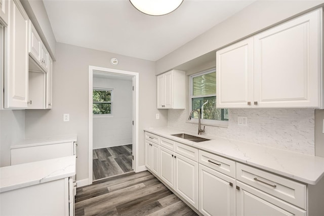 kitchen with light stone countertops, sink, white cabinets, and dark wood-type flooring