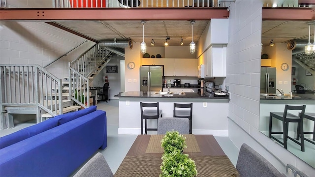 kitchen featuring white cabinets, stainless steel fridge with ice dispenser, hanging light fixtures, and a high ceiling