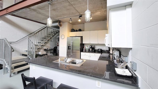 kitchen featuring sink, kitchen peninsula, stainless steel fridge, dark stone counters, and pendant lighting