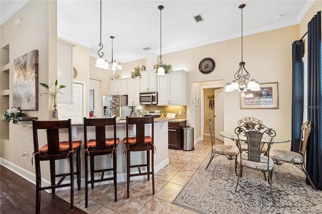 kitchen featuring a kitchen bar, stainless steel appliances, an inviting chandelier, white cabinets, and hanging light fixtures