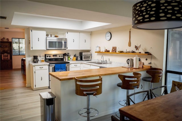 kitchen with appliances with stainless steel finishes, light wood-type flooring, white cabinetry, and a kitchen breakfast bar