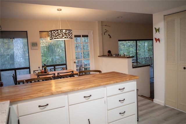 kitchen with a healthy amount of sunlight, white cabinetry, hanging light fixtures, and butcher block counters