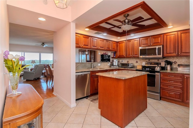 kitchen with sink, light stone countertops, appliances with stainless steel finishes, a tray ceiling, and a kitchen island