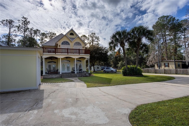 view of front of property featuring a front yard, french doors, ceiling fan, a balcony, and covered porch