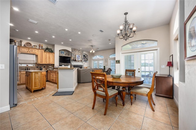 tiled dining space featuring a stone fireplace, french doors, and ceiling fan with notable chandelier