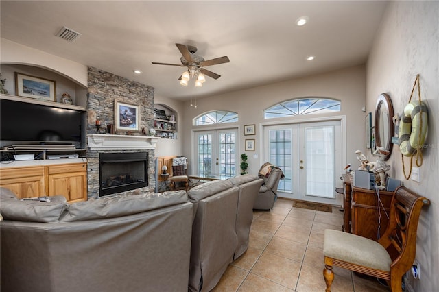 living room featuring a stone fireplace, ceiling fan, french doors, and light tile patterned flooring