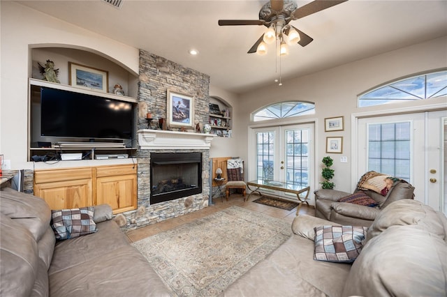 living room with tile patterned flooring, ceiling fan, a stone fireplace, and french doors