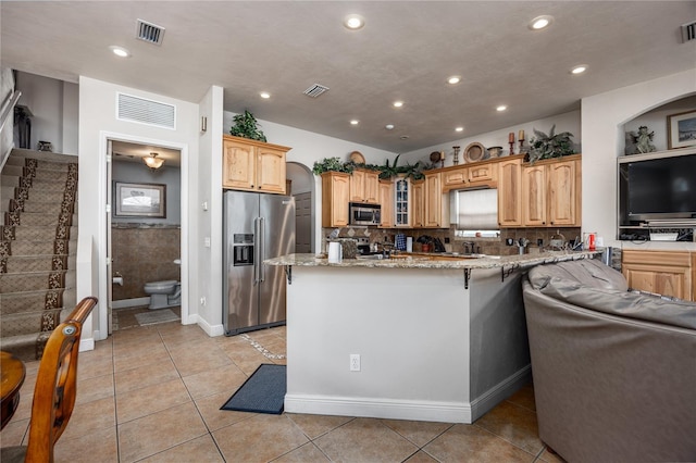 kitchen featuring decorative backsplash, light stone countertops, light tile patterned floors, kitchen peninsula, and stainless steel appliances