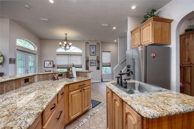 kitchen with an inviting chandelier, a center island with sink, sink, high quality fridge, and light stone counters