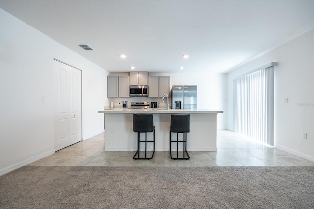 kitchen with gray cabinets, a kitchen bar, an island with sink, and appliances with stainless steel finishes