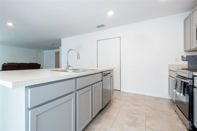 kitchen featuring gray cabinetry, a kitchen island with sink, sink, light tile patterned floors, and appliances with stainless steel finishes